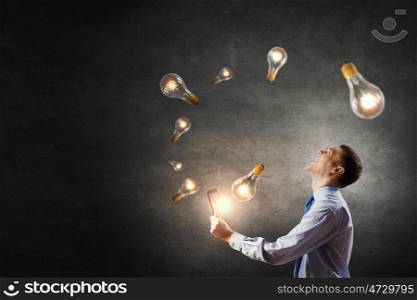 Businessman with tablet. Young businessman using tablet pc with glass lightbulbs flying out