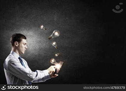 Businessman with tablet. Young businessman using tablet pc with glass lightbulbs flying out