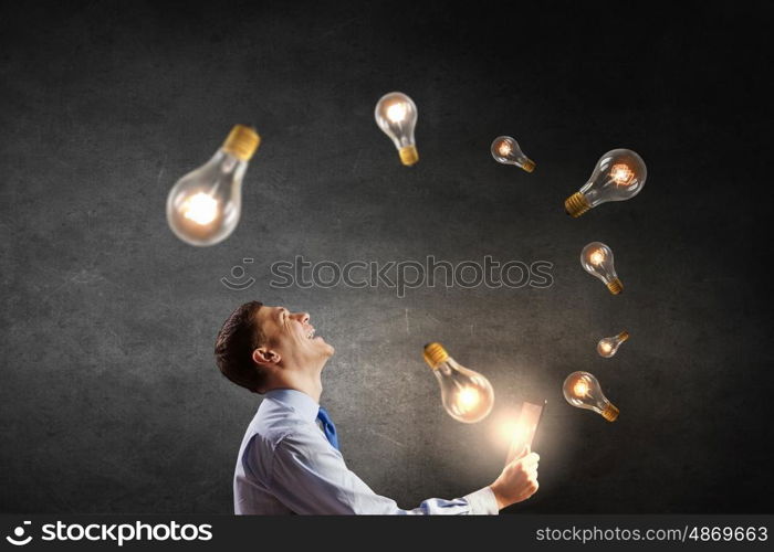 Businessman with tablet. Young businessman using tablet pc with glass lightbulbs flying out