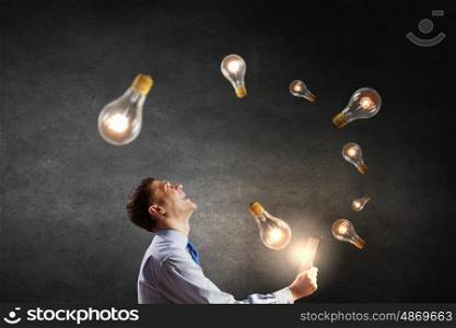 Businessman with tablet. Young businessman using tablet pc with glass lightbulbs flying out