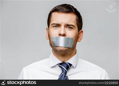 businessman with tape sealed mouth on grey background with copy space. businessman with tape sealed mouth