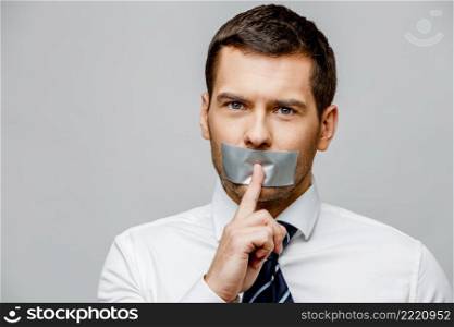 businessman with tape sealed mouth on grey background with copy space. businessman with tape sealed mouth