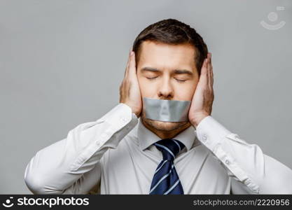 businessman with tape sealed mouth on grey background with copy space. businessman with tape sealed mouth