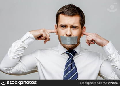 businessman with tape sealed mouth on grey background with copy space. businessman with tape sealed mouth