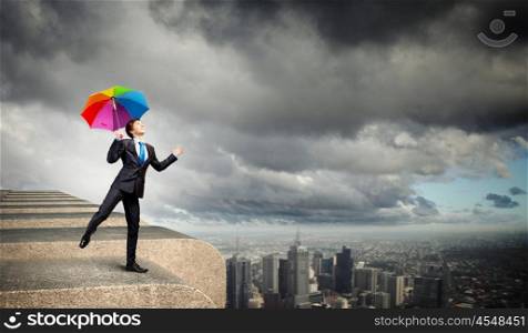 Businessman with umbrella atop of building. Businessman in black suit with umbrella atop of building