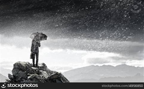 Businessman with umbrella. Back view of businessman with umbrella and suitcase standing on mountain top