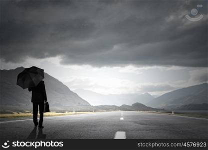 Businessman with umbrella. Back view of businessman with umbrella and suitcase walking on road