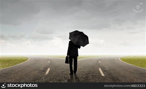 Businessman with umbrella. Back view of businessman with umbrella and suitcase walking on road