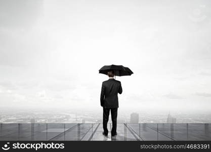 Businessman with umbrella. Back view of businessman with umbrella looking at city