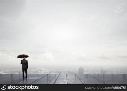 Businessman with umbrella. Back view of businessman with umbrella looking at city