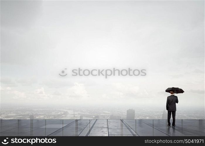 Businessman with umbrella. Back view of businessman with umbrella looking at city