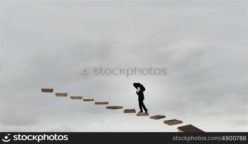 Businessman with umbrella. Businessman holding umbrella and waking on career ladder made of books