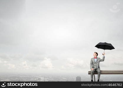 Businessman with umbrella. Young man in suit sitting with black umbrella in hands