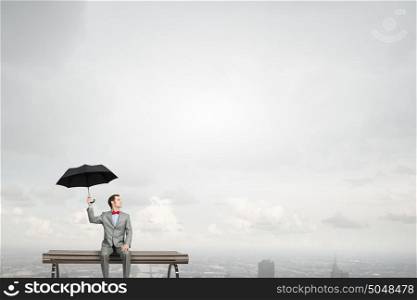 Businessman with umbrella. Young man in suit sitting with black umbrella in hands
