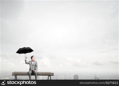 Businessman with umbrella. Young man in suit sitting with black umbrella in hands