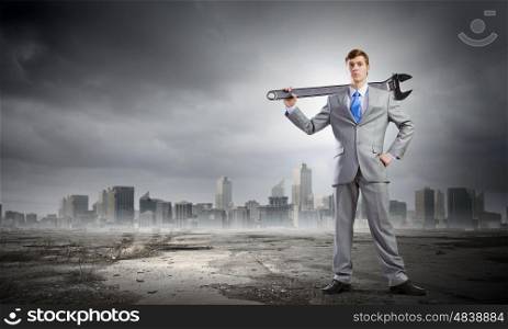Businessman with wrench. Young determined businessman with wrench in hands