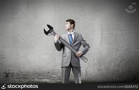 Businessman with wrench. Young determined businessman with wrench in hands