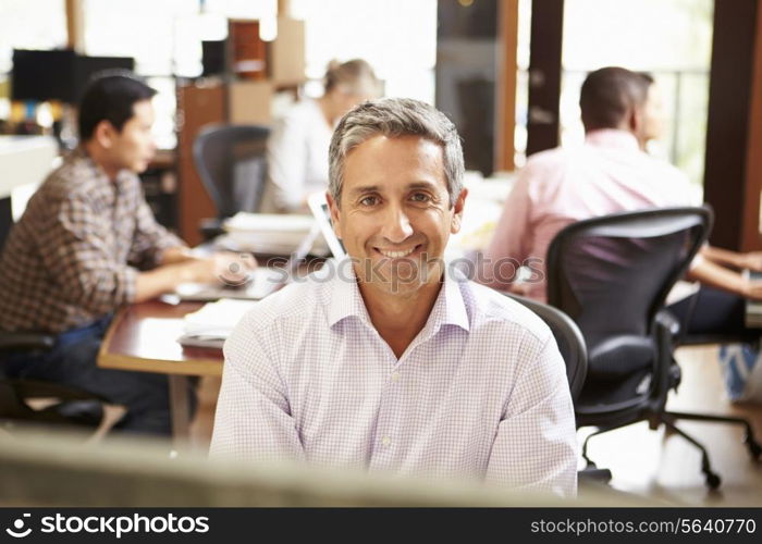 Businessman Working At Desk With Meeting In Background