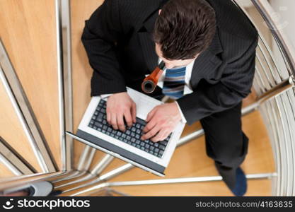 Businessman working at home with his laptop sitting on the stairs in his apartment