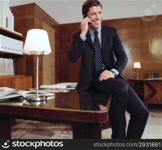 Businessman working at office desk, talking on mobile phone