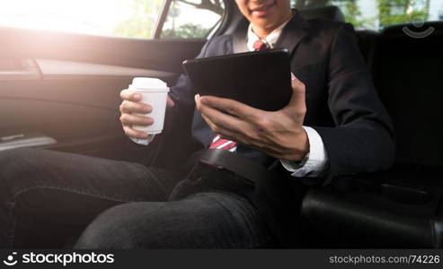 businessman working in a car and using a tablet while drinking coffee