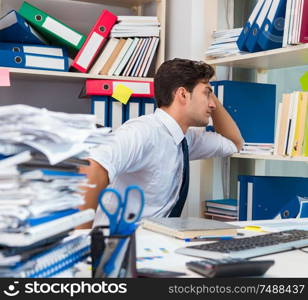 Businessman working in the office with piles of books and papers doing paperwork. Businessman working in the office with piles of books and papers