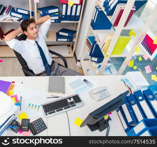 Businessman working in the office with piles of books and papers doing paperwork. Businessman working in the office with piles of books and papers