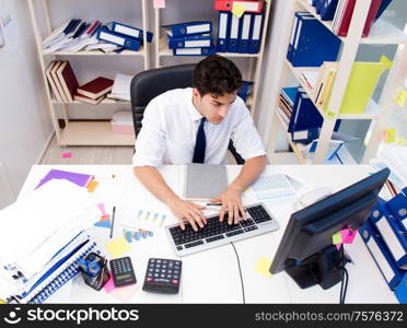 Businessman working in the office with piles of books and papers doing paperwork. Businessman working in the office with piles of books and papers