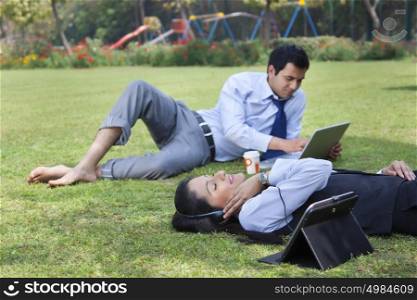 Businessman working in the park while businesswoman relaxes