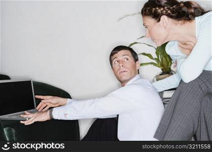 Businessman working on a laptop and looking at a businesswoman