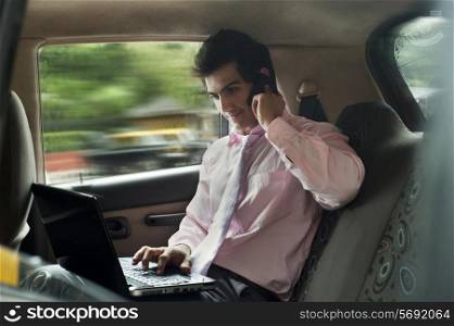 Businessman working on a laptop while talking on a mobile phone