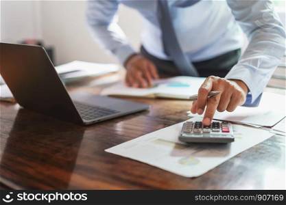 businessman working on desk office with using a calculator to calculate money report, finance accounting concept