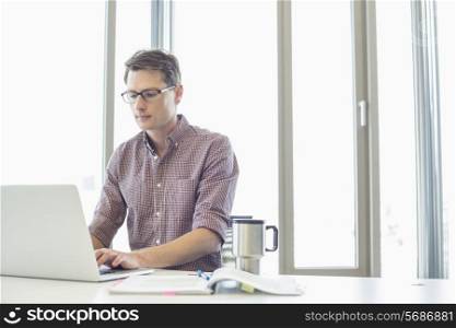 Businessman working on laptop at desk in creative office