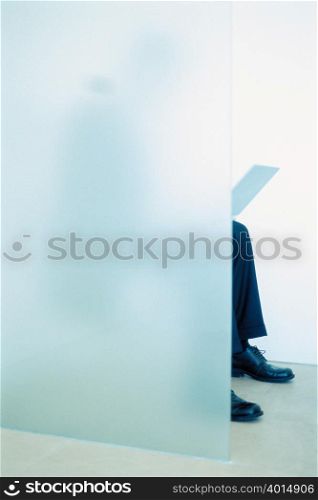 Businessman working on laptop behind glass