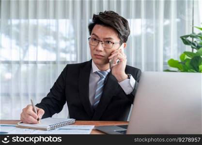 Businessman working on laptop for on office desk workspace with his smartphone. Smart executive researching financial business data or planning strategic business, talking on phone. Jubilant. Businessman working on laptop at office desk and talking on the phone. Jubilant