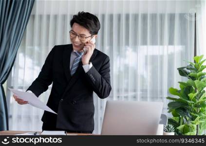 Businessman working on laptop for on office desk workspace with his smartphone. Smart executive researching financial business data or planning strategic business, talking on phone. Jubilant. Businessman working on laptop at office desk and talking on the phone. Jubilant