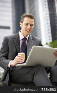 Businessman Working On Laptop Outside Office With Takeaway Coffee