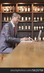 Businessman Working on Laptop, Wine Shelf in the Background