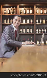 Businessman Working on Laptop, Wine Shelf in the Background