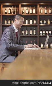 Businessman Working on Laptop, Wine Shelf in the Background