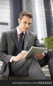 Businessman Working On Tablet Computer Outside Office With Takeaway Coffee