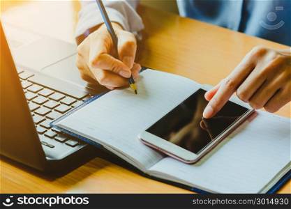 Businessman working with smart phone and laptop computer on wooden desk ; remote working concept; home business concept.