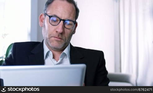Businessman working with tablet PC / ipad in his office or Hotel room while screen reflects in his glasses - tracking shot