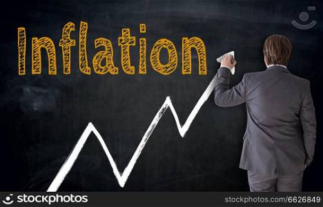 Businessman writes inflation on blackboard concept.. Businessman writes inflation on blackboard concept 