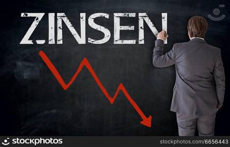 Businessman writes Zinsen (in german interest) on blackboard concept.. Businessman writes Zinsen (in german interest) on blackboard concept