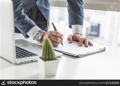 businessman writing document with pen desk with laptop