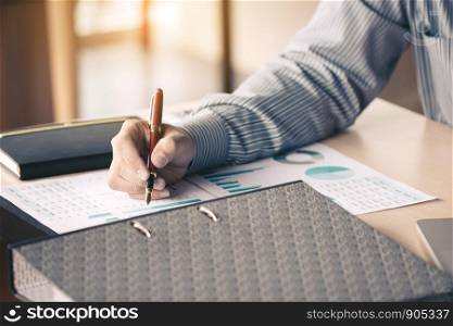 Businessman writing make note on paperwork chart summary report graph on desk for analyze data.