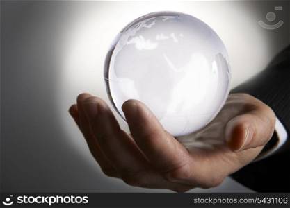 Businessmans hand holding glowing glass globe in palm against grey background