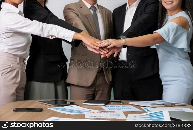 Businessmen and businesswomen putting hands together showing teamwork, support and unity during business meeting in office conference room. Teamwork and buisness success concept.