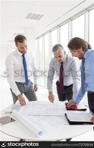 Businessmen discussing over blueprints at table in new office